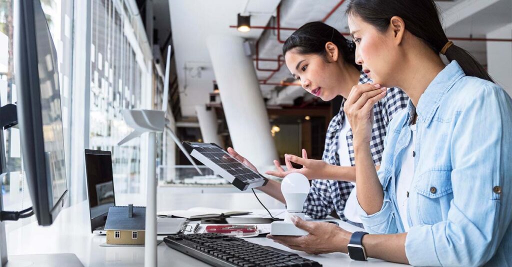 Two women sitting at a table, focused on a laptop screen.